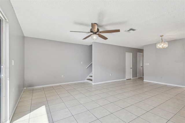 tiled empty room with a textured ceiling and ceiling fan with notable chandelier