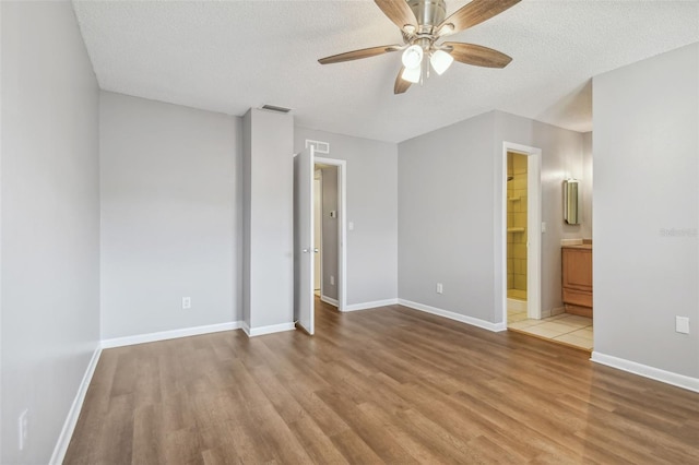 unfurnished bedroom featuring ceiling fan, light hardwood / wood-style flooring, ensuite bath, a walk in closet, and a textured ceiling