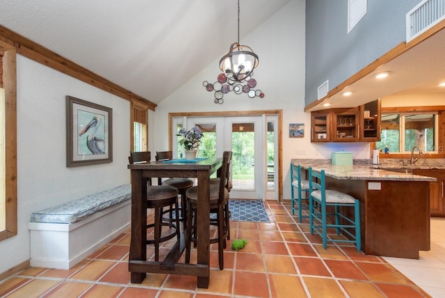 tiled dining area featuring a wealth of natural light, french doors, high vaulted ceiling, and a chandelier