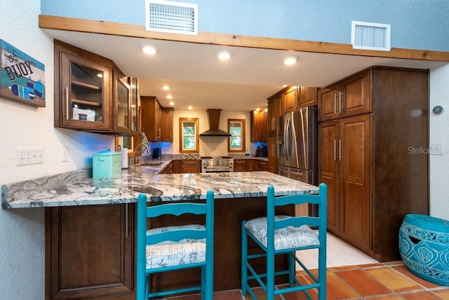 kitchen featuring a kitchen breakfast bar, wall chimney range hood, sink, kitchen peninsula, and stainless steel appliances