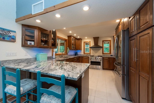 kitchen with wall chimney exhaust hood, light stone countertops, kitchen peninsula, and stainless steel appliances