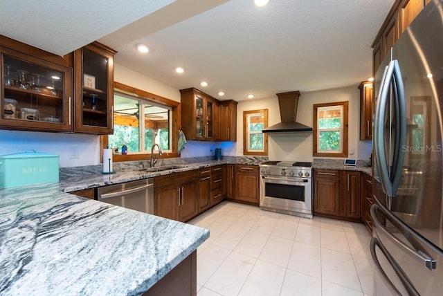 kitchen featuring kitchen peninsula, light stone counters, wall chimney exhaust hood, stainless steel appliances, and sink