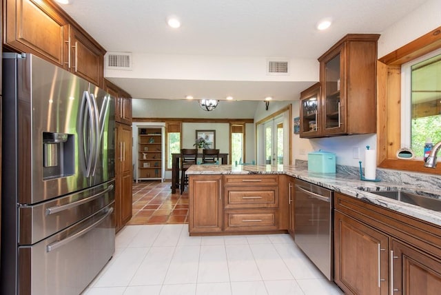 kitchen featuring kitchen peninsula, light stone countertops, stainless steel appliances, sink, and a notable chandelier