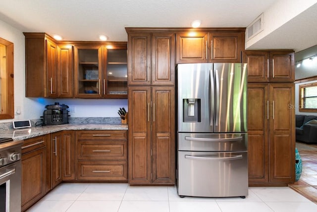 kitchen with light stone countertops, light tile patterned floors, stainless steel appliances, and a textured ceiling