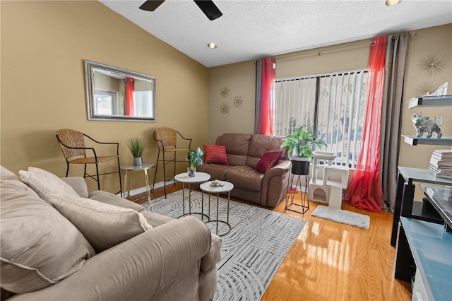 living room with light wood-type flooring, lofted ceiling, ceiling fan, and a textured ceiling