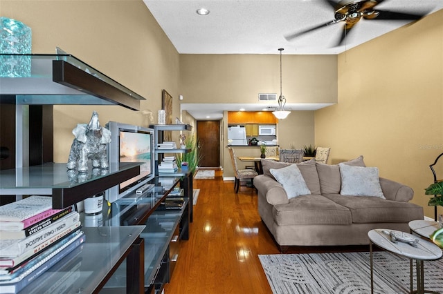 living room with ceiling fan, a textured ceiling, and dark wood-type flooring