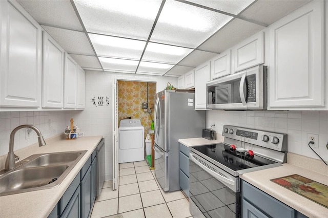 kitchen with appliances with stainless steel finishes, white cabinetry, sink, and washer / dryer