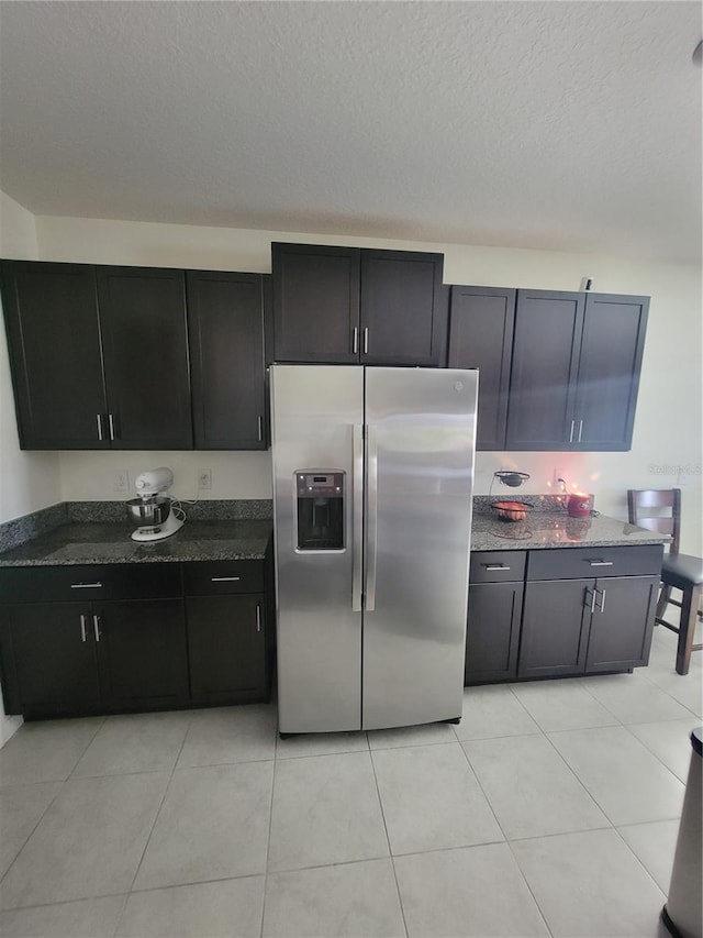 kitchen with light tile patterned floors, a textured ceiling, stainless steel fridge with ice dispenser, and dark stone counters