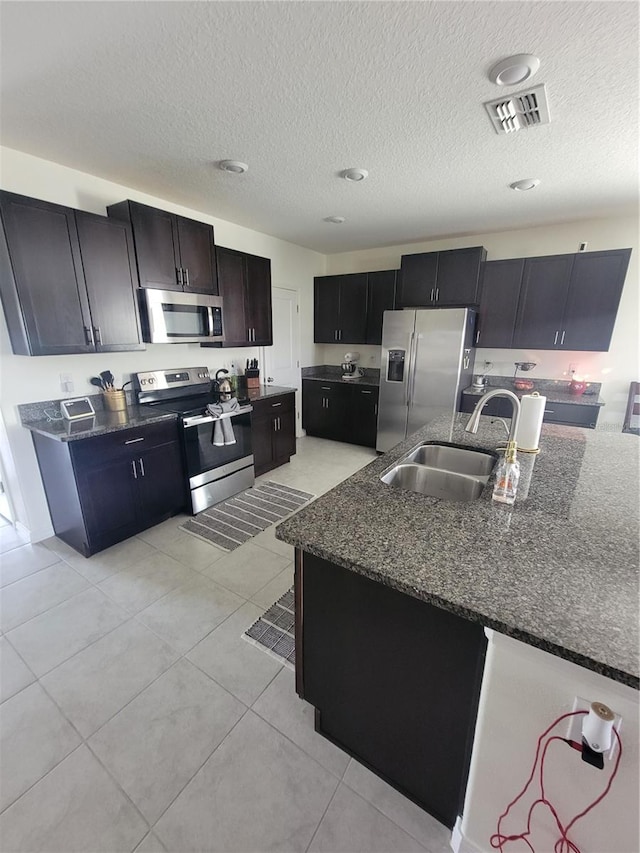 kitchen featuring a textured ceiling, light tile patterned flooring, sink, appliances with stainless steel finishes, and dark stone countertops