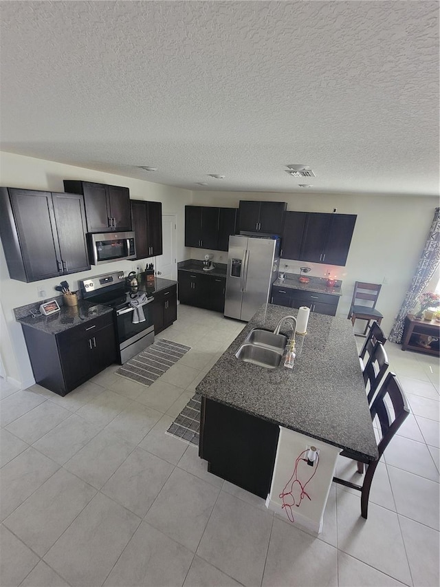 kitchen with light tile patterned floors, sink, a textured ceiling, a kitchen island with sink, and appliances with stainless steel finishes