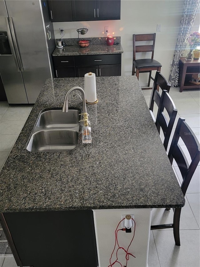 kitchen with light tile patterned floors, dark stone countertops, sink, and stainless steel fridge with ice dispenser