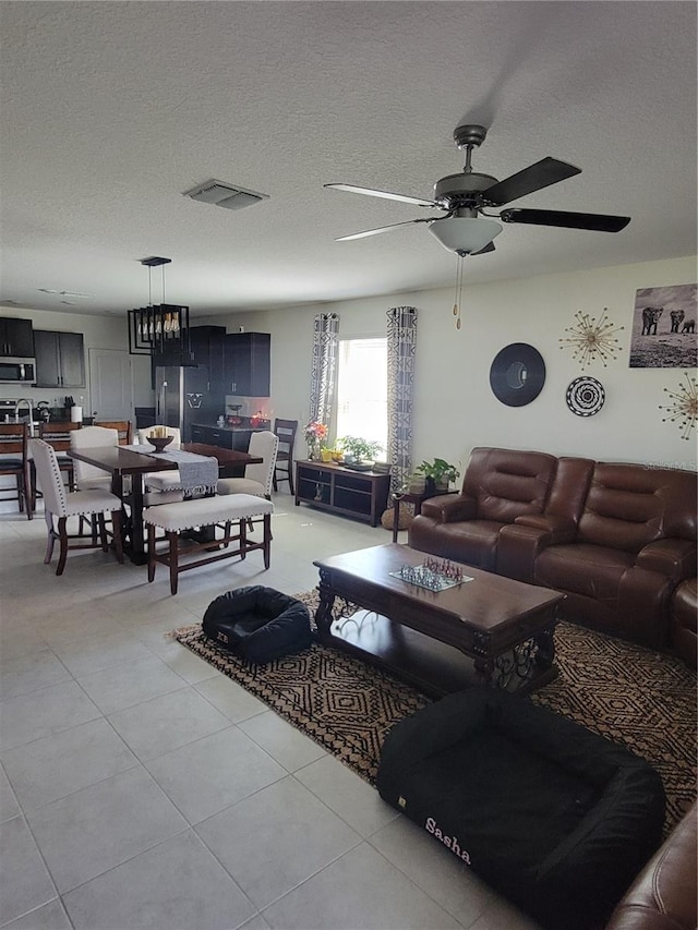 tiled living room featuring a textured ceiling and ceiling fan with notable chandelier