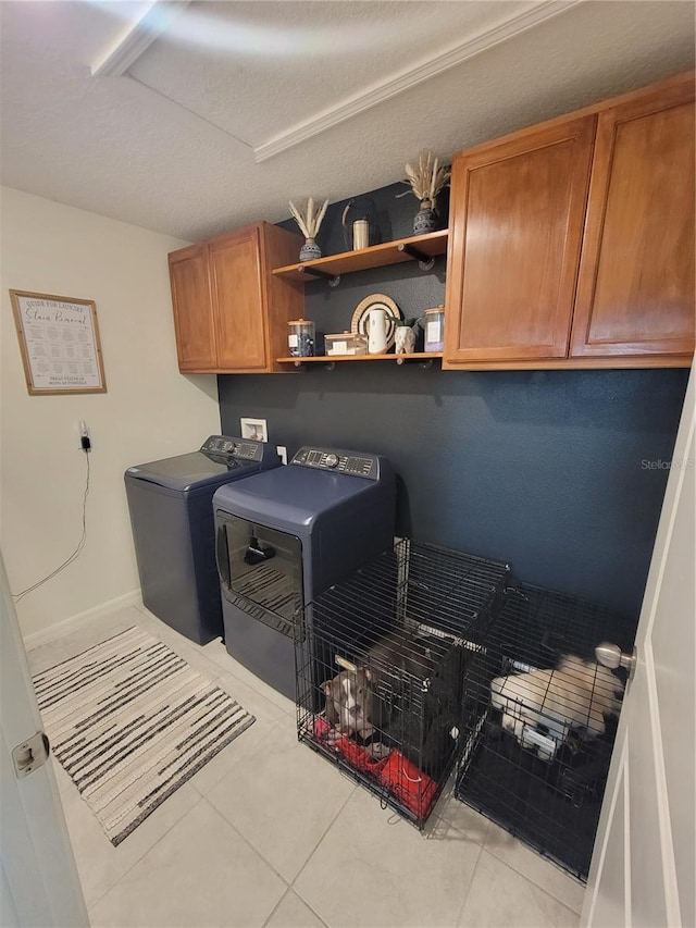 laundry area featuring cabinets, a textured ceiling, washing machine and clothes dryer, and light tile patterned flooring