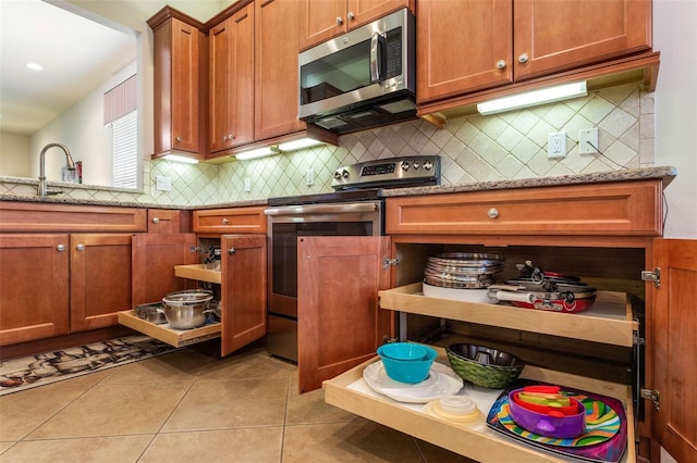 kitchen with light stone counters, sink, stainless steel appliances, backsplash, and light tile patterned floors