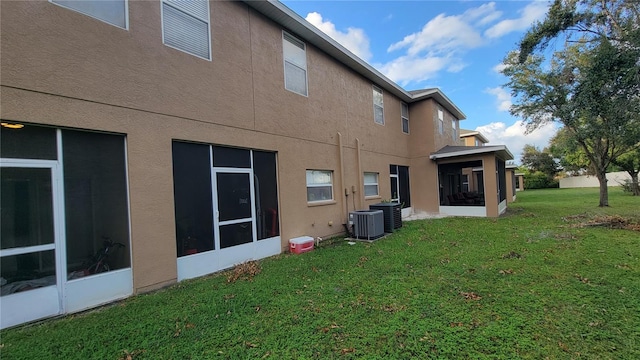 exterior space featuring a sunroom, central AC unit, and a lawn