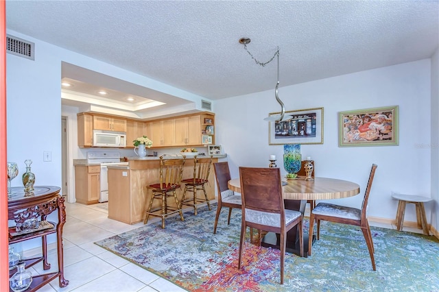 dining room with a textured ceiling, a raised ceiling, and light tile patterned floors