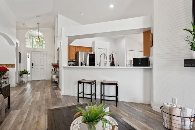 kitchen featuring stainless steel fridge, light hardwood / wood-style floors, high vaulted ceiling, kitchen peninsula, and sink