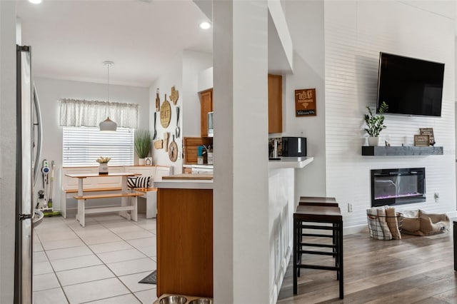 kitchen with hanging light fixtures, a large fireplace, stainless steel fridge, and light hardwood / wood-style flooring