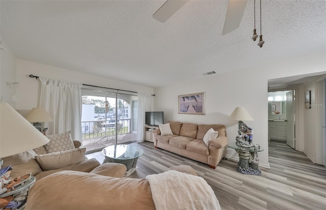 living room with ceiling fan, a textured ceiling, and light hardwood / wood-style flooring