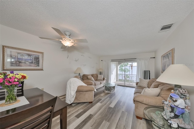 living room featuring light wood-type flooring, a textured ceiling, and ceiling fan