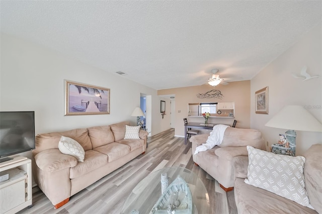 living room with light wood-type flooring, ceiling fan, and a textured ceiling