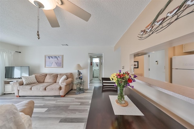 living room featuring vaulted ceiling, light hardwood / wood-style floors, ceiling fan, and a textured ceiling