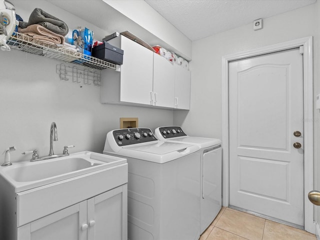 laundry room with cabinets, a textured ceiling, sink, light tile patterned floors, and washing machine and dryer