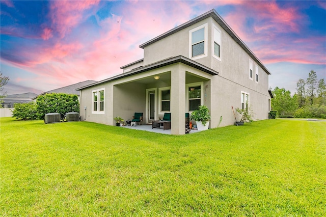 back house at dusk with a patio, central AC unit, and a lawn