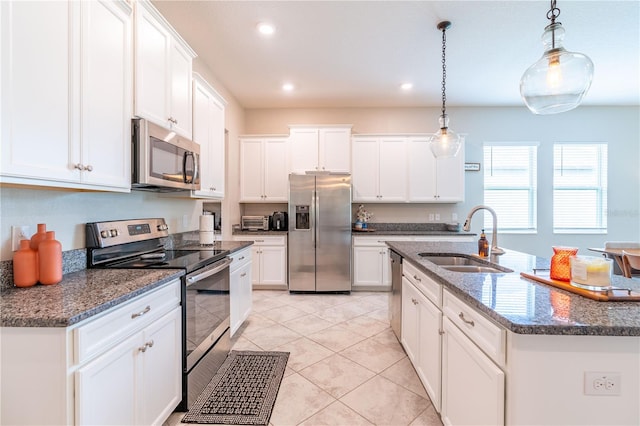 kitchen with decorative light fixtures, sink, white cabinets, stainless steel appliances, and a center island with sink