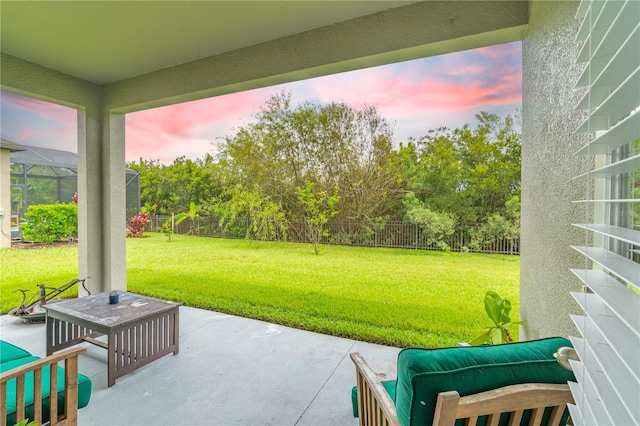 patio terrace at dusk featuring a lanai and a lawn