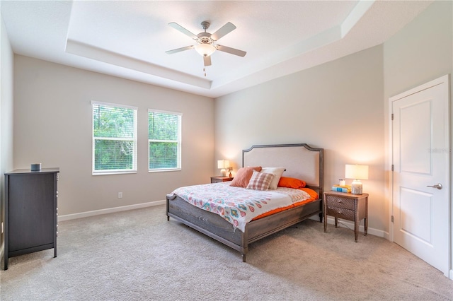 carpeted bedroom with a tray ceiling and ceiling fan