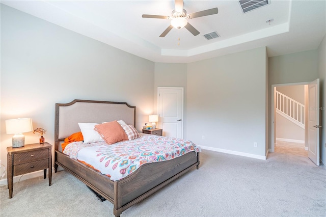 bedroom with ceiling fan, a raised ceiling, and light carpet