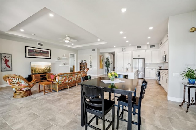 dining area with ceiling fan, a tray ceiling, and sink