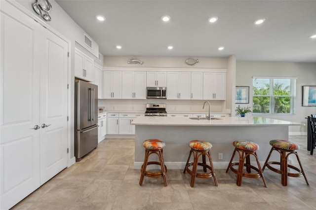 kitchen with an island with sink, stainless steel appliances, white cabinets, and a breakfast bar area