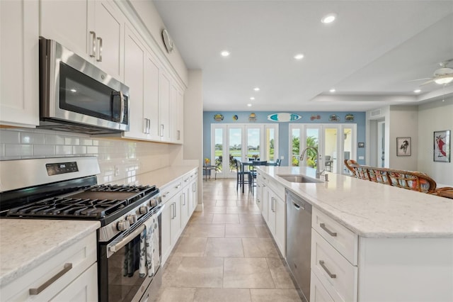 kitchen with appliances with stainless steel finishes, an island with sink, white cabinets, french doors, and sink