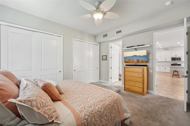 carpeted bedroom with ceiling fan and multiple closets