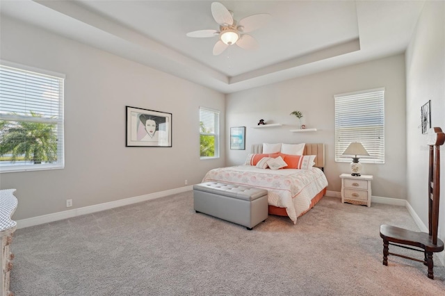 bedroom featuring a raised ceiling, ceiling fan, and light colored carpet