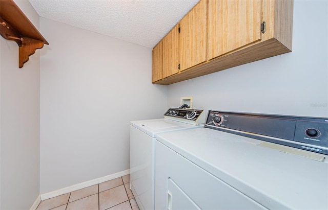 laundry room featuring light tile patterned floors, washing machine and dryer, cabinets, and a textured ceiling