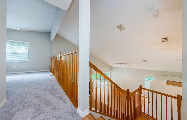 corridor with light carpet, vaulted ceiling, rail lighting, and a textured ceiling