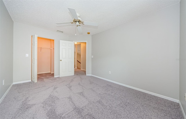 unfurnished bedroom with a walk in closet, light carpet, a textured ceiling, a closet, and ceiling fan