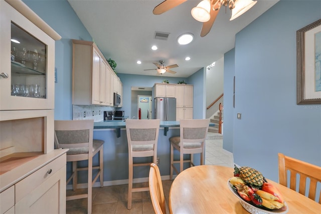 kitchen featuring ceiling fan, light tile patterned flooring, tasteful backsplash, stainless steel appliances, and a kitchen bar