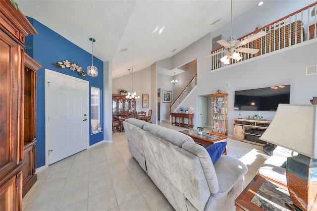 tiled living room with ceiling fan with notable chandelier and high vaulted ceiling