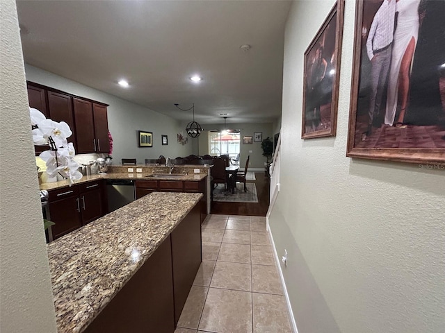 kitchen with kitchen peninsula, stone countertops, light tile patterned floors, decorative light fixtures, and stainless steel dishwasher