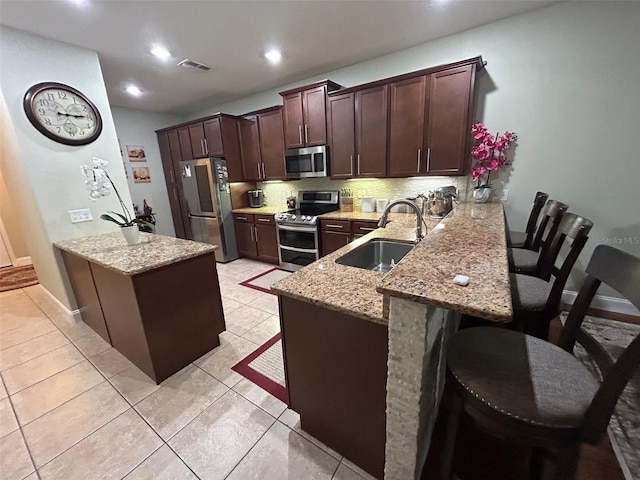 kitchen with a kitchen breakfast bar, tasteful backsplash, kitchen peninsula, stainless steel appliances, and sink