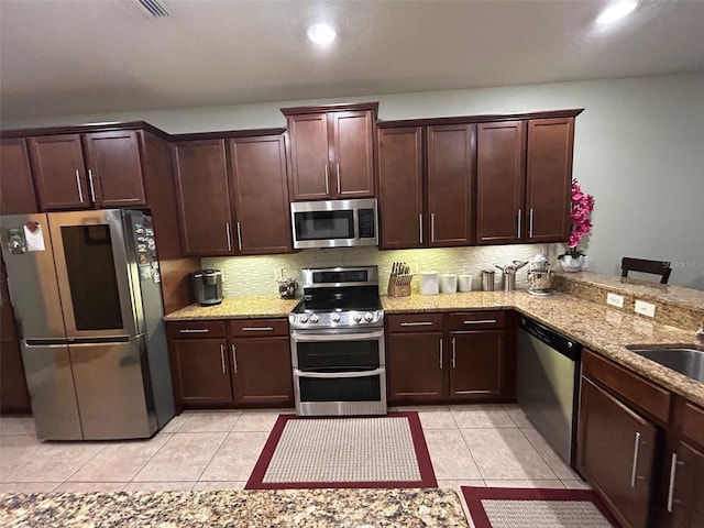 kitchen featuring light tile patterned floors, kitchen peninsula, tasteful backsplash, appliances with stainless steel finishes, and light stone countertops