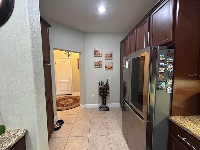 kitchen with light stone countertops, dark brown cabinets, light tile patterned floors, and stainless steel refrigerator