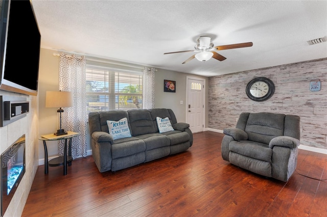 living room with ceiling fan, a textured ceiling, dark hardwood / wood-style floors, and a tiled fireplace