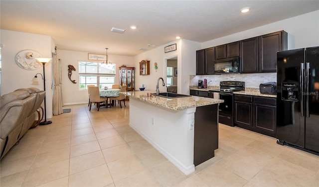 kitchen with pendant lighting, light stone counters, a kitchen island with sink, decorative backsplash, and black appliances