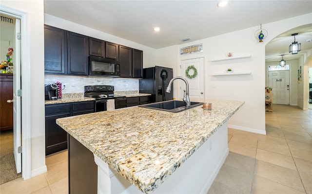 kitchen featuring light tile patterned floors, tasteful backsplash, arched walkways, black appliances, and a sink