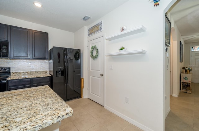 kitchen featuring light tile patterned flooring, backsplash, black appliances, light stone countertops, and dark brown cabinets